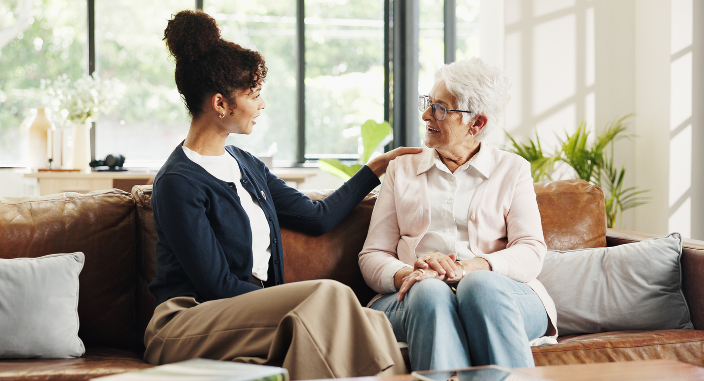 A younger woman sitting beside an older woman on a sofa, talking warmly